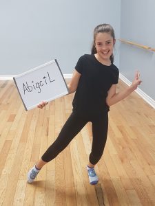 Girl making smiling and holding a white board with her name, Abigail, written on it.