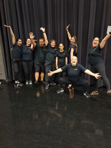 Several DAM team members wearing black Dance Ability movement volunteer t-shirts raising their arms and looking excited