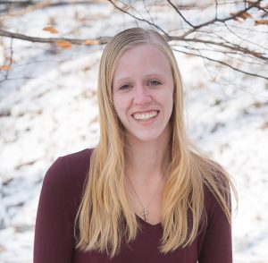 Young blond woman smiling at the camera. There is snow on the background