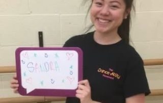 Sandra smiles and holds a whiteboard with her name.