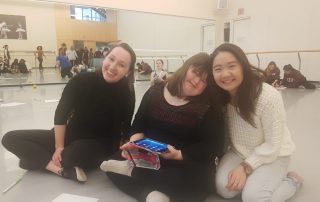 Three girls smiling. The one in the middle is holding an iPad.