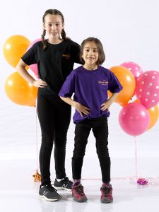 Dancer and dance buddy wearing dance ability t-shirts pose with hands on waist in front of pink and orange balloons.
