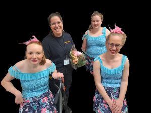 OT Emma stands smiling with three dancers in costumes next to her (one using a walker).